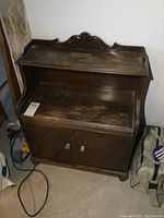 Front view of the small wood cabinet showing worn finish and two doors with knobs.