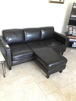 Black vinyl sofa set with chaise positioned in center, showing front left angled view on tile floor.