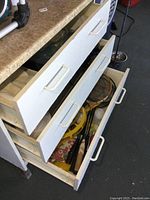 Photo showing three white drawers partially open revealing various sports and kitchen items including badminton rackets and frisbees.