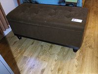 Full view of the vintage brown upholstered storage bench showing tufted top, rectangular shape, and wooden legs.
