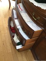 Three wooden drawers filled with folded linens, showing a variety of colors including white, red, and cream crochet pieces.