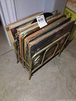 Photo showing small metal rack filled with various vintage vinyl LP records including rock n roll albums. Rack and records show aged wear.