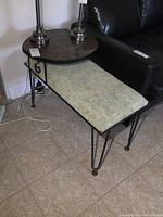 Side angle showing the vintage wrought iron frame, upholstered green seat section and the scalloped dark brown melamine top with twisted legs.