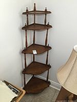 Full view of the five-tier wooden corner what not shelf placed in a corner, showing its height and design.