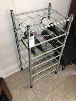 Metal wine bottle rack shown with wine bottles stored horizontally, floor and wall visible.