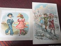 Photo showcasing two antique Lion Coffee advertising cards featuring children at play; one with a boy and girl holding hands by the seaside.