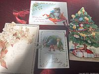 Photo showing four antique Christmas cards spread out on a surface, including the Christmas tree shaped booklet style card and floral embossed card.