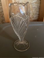 Side view of clear pressed glass bud vase showing leaf and fan pattern and scalloped rim.