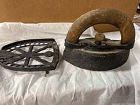 Photo showing antique sad iron with wooden handle and metal base, and the metal trivet placed beside it.