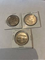 Three Canadian dollar coins in holders: top two are 1982 Confederation commemoratives, bottom one is 1968 Voyageur dollar