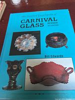 Front cover of the encyclopedia showing three different carnival glass pieces: a spiked round bowl, a round lidded dish with feet, and a dark iridescent vase.