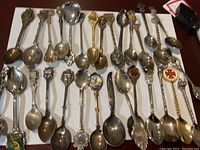 Overview of all 29 vintage souvenir spoons displayed on a white surface showing varied international designs and metals