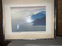 Full view of framed print depicting layered coastal hills in blues and grays, titled 'Sunshine Coast' and signed by the artist.