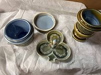 Overview of the three pottery pieces laid on cloth: lidded pot with blue interior, shamrock dish with leprechaun figurine, and small urn.