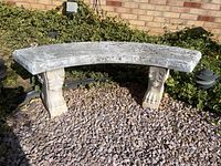 Full view of curved cement bench outdoors on gravel with mildew and weathering visible.