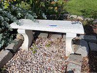 Full view of the cement bench outdoors showing the complete bench structure with seat and legs, placed on gravel ground near plants.