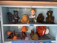 Shelf with squirrel, three frog figurines including one large yellow and two dark green frogs, and fisherman figurine holding fish.