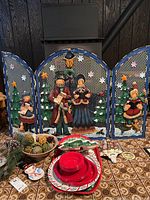 Full frontal view of the three-panel Christmas-themed metal fireplace screen with assorted holiday decorations and picnic ware in front.