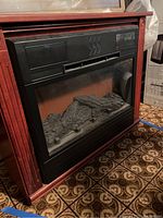 Front angled view of electric fireplace heater with wood surround showing faux logs and glass front panel.