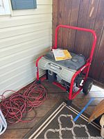 Generator on deck with red frame, gray housing, black fuel tank and two red extension cords coiled beside it