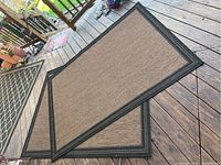 Two matching brown and black bordered rugs lying partially overlapped on wooden floor.