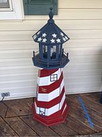 Overall front and side view of the tall red, white, and blue wooden lighthouse with star decorations on the top.