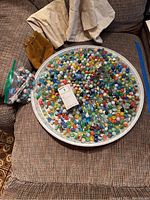 Wide view showing the large metal tray filled with assorted glass marbles, plastic bag with additional marbles, and cloth bags in background