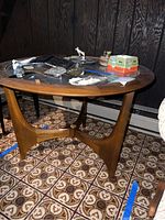 Mid-century modern round side table with wood frame and glass top shown from an angle with items on top.