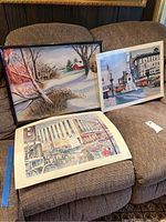 Photo showing all three items: the framed original painting and two unframed art prints displayed on a couch.