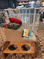 Photo of beige plastic pet steps with two carpeted steps and wooden framed bowl holder with two circular cutouts for bowls, placed on carpet.