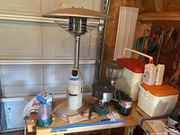 Photo showing Dyna-Glo propane heater, two Coleman lanterns, two coolers, lighter fluid, and propane cans on a workbench.