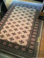 Full view of the rectangular area rug laid on a hardwood floor showing the overall pattern and fringe ends.