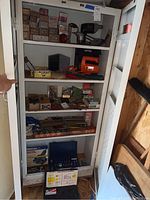Full view of metal cabinet shelves showing power tools, hand tools, and boxes of hardware items.