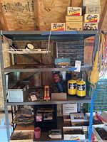 Wide shot of metal shelves holding the propane torch kit, propane tanks, various cigar boxes of nails, toolbox, ratchets, and other hardware items.