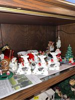 Shelf with white ceramic reindeer with gold antlers, gingerbread man, and Christmas characters including a tree and Santa Claus figurine.