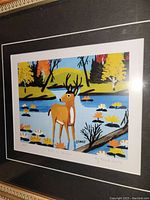 Close-up of framed limited edition Maud Lewis print showing deer in water with colorful foliage.