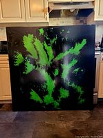 Front view of the large scale painting indoors against kitchen background, showing the bold green on black abstract artwork.