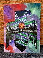 Full frontal view of the stretched and framed painting leaning against a brick wall outdoors.