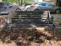 Front view of metal frame garden bench with wooden slats showing wear and dirt on ground surface.