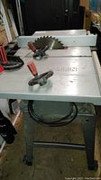 Full view of Craftsman table saw on metal stand showing saw blade, clamps, and work table surface.