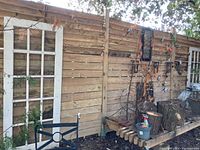 Wide view of fence showing white glass panel door, string lights, metal stars, gecko, wooden logs, and garden tools.