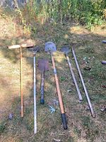 Overview of all six garden tools laid out on grass showing broom, rakes, and shovels
