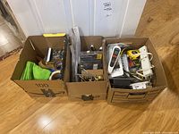 Three cardboard boxes filled with assorted hardware including vent covers, power bars, doorknobs, and miscellaneous items.