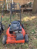 Front view of orange Kohler lawnmower on grass with black engine cover and handlebar.
