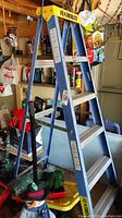 Full view of the Featherlite ladder showing blue metal legs and yellow plastic top platform, four steps visible, some scratches present.