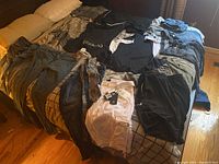 Full assortment of men's pants and shorts laid out flat on bed including denim and casual fabrics, mostly dark colors.