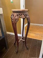 Full view of the tall wooden plant stand showing curved legs and decorative carving beneath marble top.