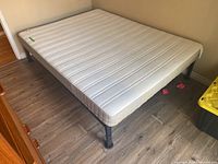 Queen size bed frame with mattress from corner angle showing mattress texture and bed legs.