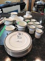 Set of Royal Doulton Ravenswood china pieces on dark surface, showing cups, saucers, plates, and demitasse cups with decorative silver or platinum rim.