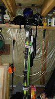 Overall shot showing three helmets, skis, ski poles, boots, and other items in storage.